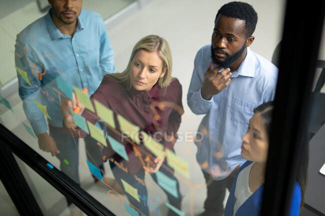 Diversos colegas de negócios masculinos e femininos lendo notas coloridas na parede de vidro. trabalhando em negócios em um escritório moderno. — Fotografia de Stock