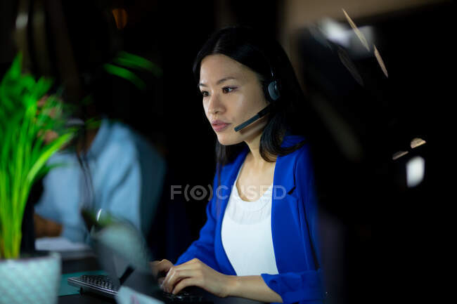Mujer de negocios asiática que trabaja de noche con auriculares. trabajar hasta tarde en los negocios en una oficina moderna. - foto de stock