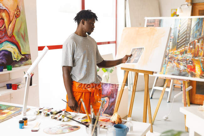 Pintor afro-americano no trabalho segurando foto no estúdio de arte. criação e inspiração em um estúdio de pintura de artistas. — Fotografia de Stock