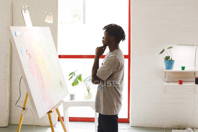 Afrikanischer männlicher Maler bei der Arbeit und betrachtet Kunstwerke im Kunstatelier. Kreation und Inspiration im Malatelier eines Künstlers. — Stockfoto