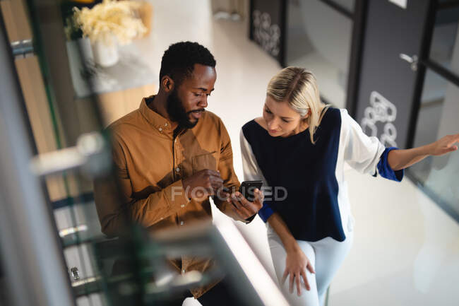 Zwei unterschiedliche männliche und weibliche Geschäftskollegen, die miteinander reden und das Smartphone benutzen. Arbeit in einem modernen Büro. — Stockfoto