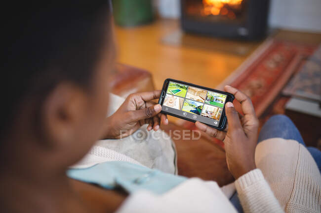 Femme afro-américaine dans le salon assis sur un canapé et utilisant un smartphone. mode de vie domestique, profiter du temps libre à la maison. — Photo de stock