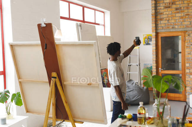 Африканський американський художник-чоловік на роботі фотографує роботи зі смартфоном у художній студії. Творіння та натхнення у художній майстерні. — стокове фото