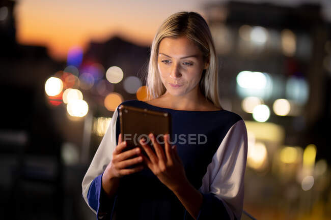 Mulher de negócios caucasiana trabalhando à noite usando tablet. trabalhando até tarde em negócios em um escritório moderno. — Fotografia de Stock