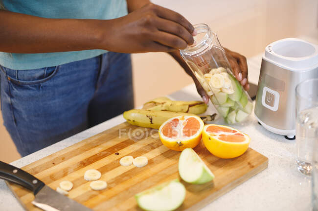 Mujer afroamericana en cocina preparando bebida saludable. estilo de vida doméstico, disfrutando del tiempo libre en casa. - foto de stock