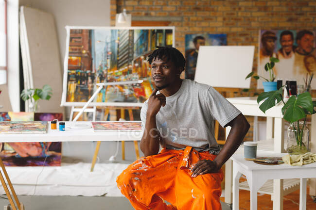 Pintor afroamericano en el trabajo sentado y pensando en el estudio de arte. creación e inspiración en un estudio de pintura de artistas. - foto de stock