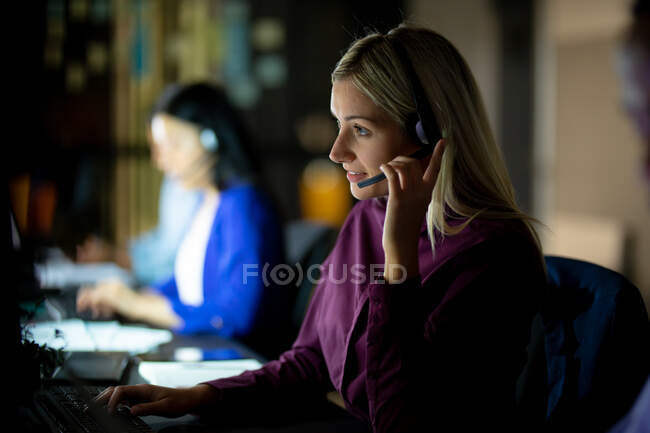Donna d'affari caucasica che lavora di notte con le cuffie. lavorare fino a tardi negli affari in un ufficio moderno. — Foto stock