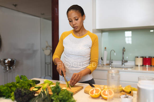 Mixed race woman standing in kitchen chopping vegetables. domestic lifestyle, enjoying leisure time at home. — Stock Photo
