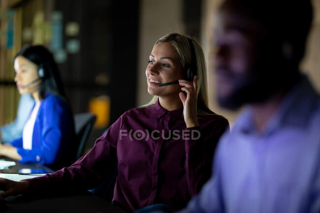Mulher de negócios caucasiana a trabalhar à noite com auscultadores. trabalhando até tarde em negócios em um escritório moderno. — Fotografia de Stock