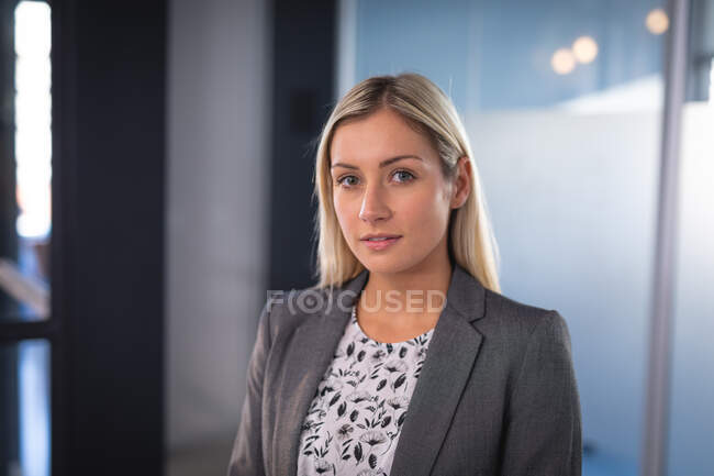 Porträt einer kaukasischen Geschäftsfrau, die eine graue Jacke trägt und in die Kamera blickt. Arbeit in einem modernen Büro. — Stockfoto