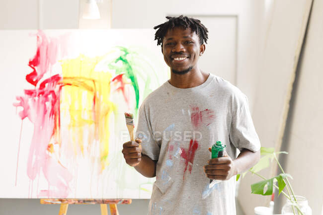Retrato de pintor americano africano no trabalho segurando pincel e pintura no estúdio de arte. criação e inspiração em um estúdio de pintura de artistas. — Fotografia de Stock