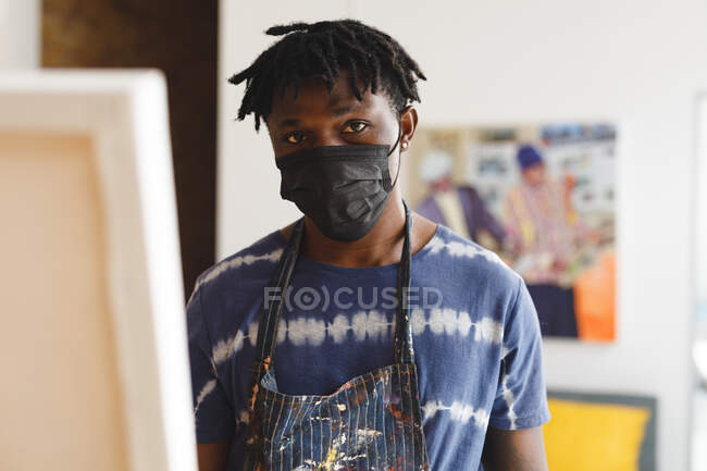 Portrait of african american male painter wearing face mask in art studio. creation and inspiration at an artists painting studio during coronavirus covid 19 pandemic. — Stock Photo