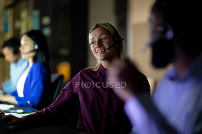 Mujer de negocios caucásica que trabaja de noche con auriculares. trabajar hasta tarde en los negocios en una oficina moderna. - foto de stock