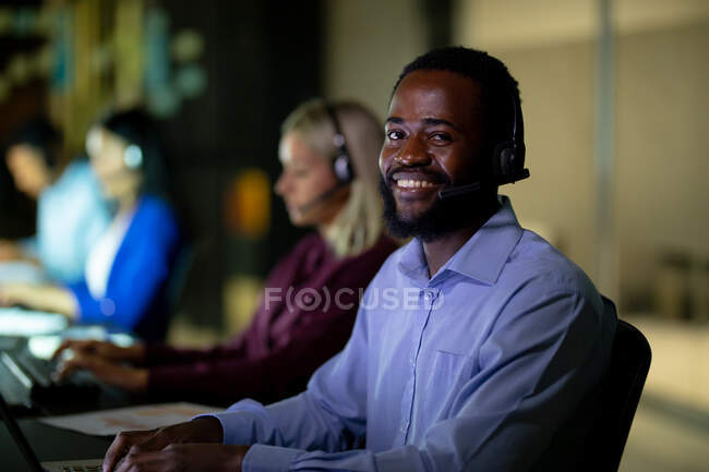 Retrato de um empresário afro-americano a trabalhar à noite com auscultadores. trabalhando até tarde em negócios em um escritório moderno. — Fotografia de Stock