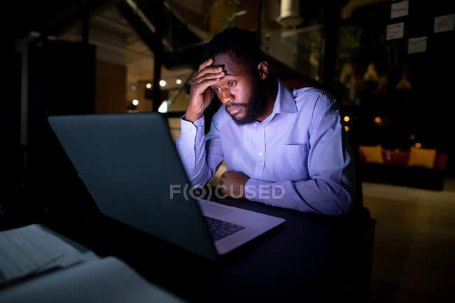 Африканский американский бизнесмен работает по ночам, сидит за столом и пользуется ноутбуком. работать допоздна в современном офисе. — стоковое фото