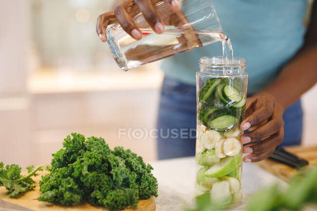 Mulher afro-americana na cozinha preparando bebida saudável. estilo de vida doméstico, desfrutando de tempo de lazer em casa. — Fotografia de Stock