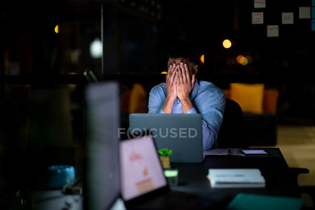 Mixed race businessman working at night, sitting at desk and using laptop. working late in business at a modern office. — Stock Photo