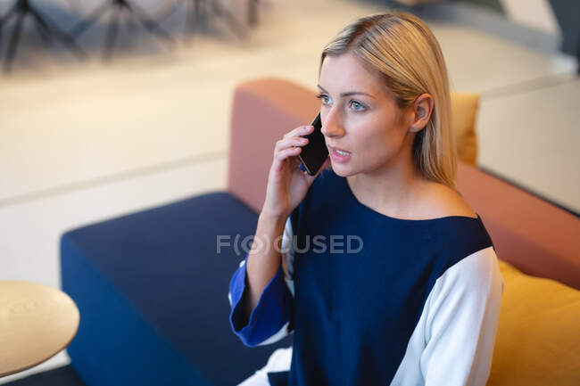 Mulher de negócios caucasiana sentada no sofá e usando smartphone. trabalhando em negócios em um escritório moderno. — Fotografia de Stock