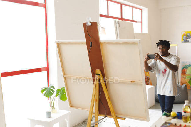 Afrikanischer männlicher Maler bei der Arbeit, der im Kunstatelier Kunstwerke mit dem Smartphone fotografiert. Kreation und Inspiration im Malatelier eines Künstlers. — Stockfoto