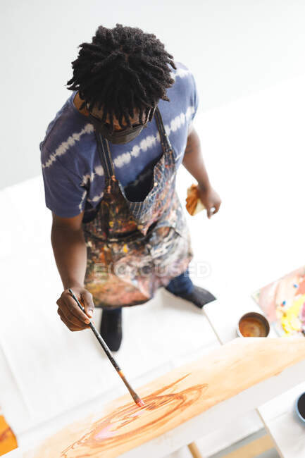 Peintre afro-américain portant un masque facial portrait sur toile dans un atelier d'art. création et inspiration dans un atelier de peinture d'artistes pendant coronavirus covid 19 pandémie. — Photo de stock