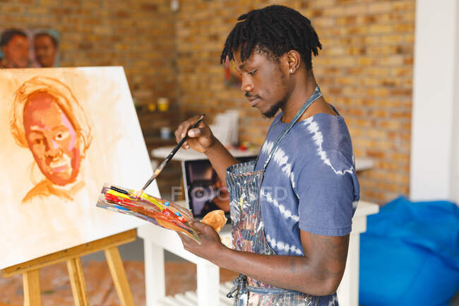 Afrikanischer männlicher Maler bei der Arbeit beim Malen von Porträt auf Leinwand im Kunstatelier. Kreation und Inspiration im Malatelier eines Künstlers. — Stockfoto