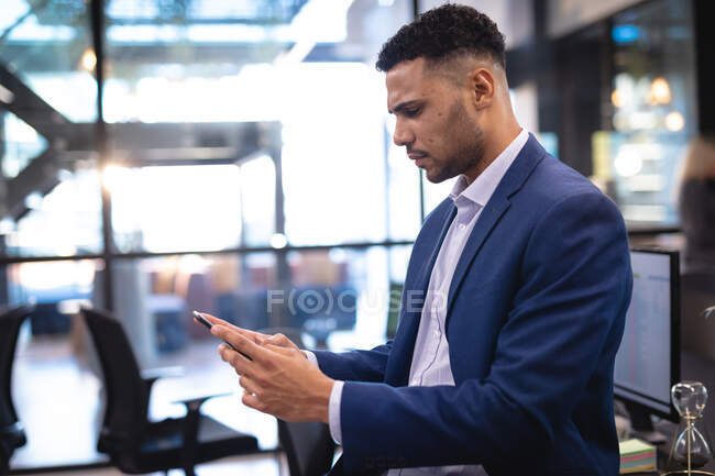 Uomo d'affari misto corsa utilizzando smartphone e seduto alla scrivania. lavorare in azienda in un ufficio moderno. — Foto stock