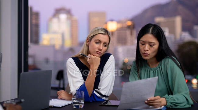 Dos compañeras de negocios diversas hablando y sosteniendo documentos. trabajar en un negocio en una oficina moderna. - foto de stock