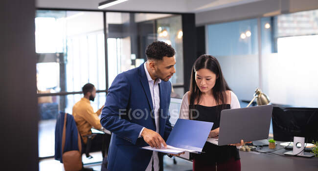 Дві різні чоловічі та жіночі бізнес-колеги використовують ноутбук та розмовляють. робота в бізнесі в сучасному офісі . — стокове фото