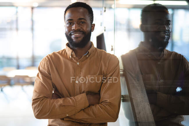 Retrato de un hombre de negocios afroamericano sonriente con los brazos cruzados mirando a la cámara. trabajar en un negocio en una oficina moderna. - foto de stock