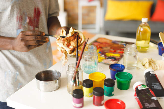 Pintor afroamericano en el trabajo limpiando pinceles en el estudio de arte. creación e inspiración en un estudio de pintura de artistas. - foto de stock