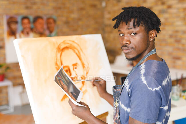 Retrato del pintor afroamericano en el trabajo pintando retrato sobre lienzo en el estudio de arte. creación e inspiración en un estudio de pintura de artistas. - foto de stock