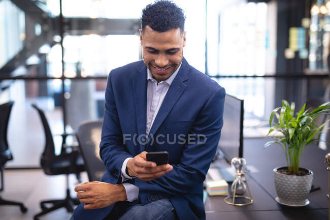 Homem de negócios de raça mista usando smartphone e sentado na mesa. trabalhando em negócios em um escritório moderno. — Fotografia de Stock