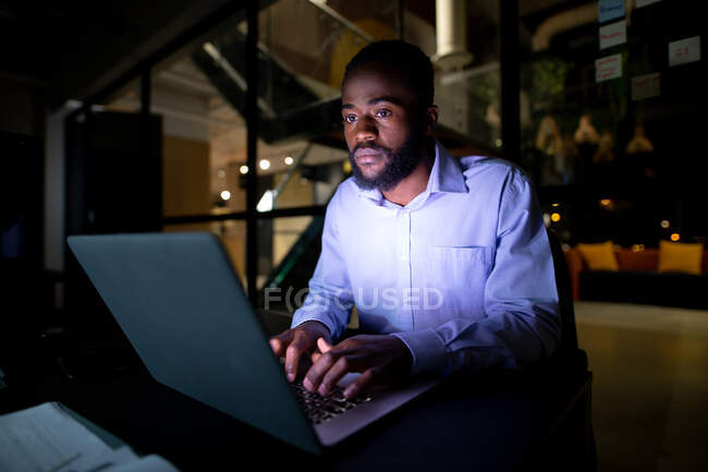 Afroamerikanischer Geschäftsmann, der nachts am Schreibtisch sitzt und Laptop benutzt. spät arbeiten in einem modernen Büro. — Stockfoto