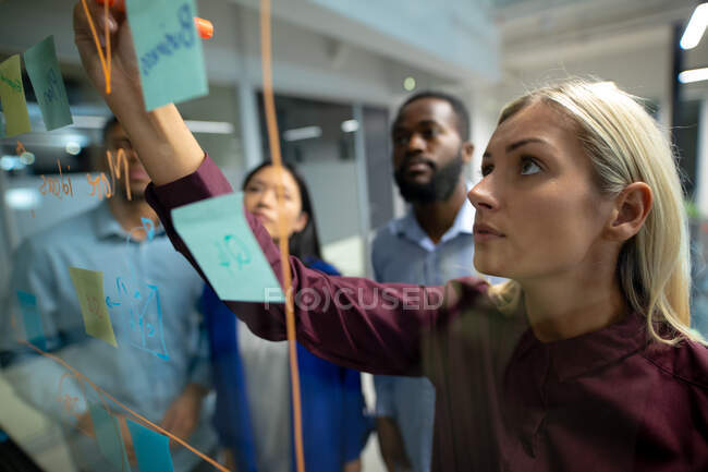 Diverse male and female business colleagues reading colourful memo notes on glass wall. working in business at a modern office. — Stock Photo