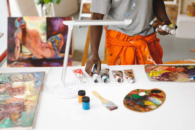 African american male painter at work holding paints in art studio. creation and inspiration at an artists painting studio. — Stock Photo