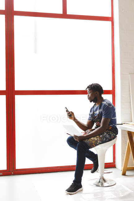 Pittore afroamericano di sesso maschile al lavoro utilizzando smartphone in studio d'arte. creazione e ispirazione in uno studio di pittura artisti. — Foto stock