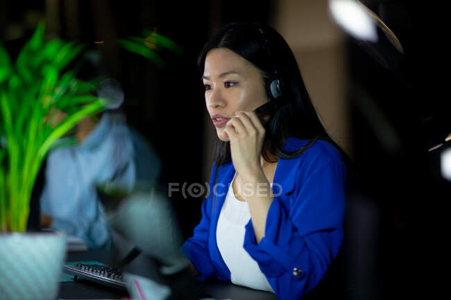 Азійська бізнесменка працює вночі в навушниках. Працював у сфері бізнесу в сучасному офісі.. — стокове фото