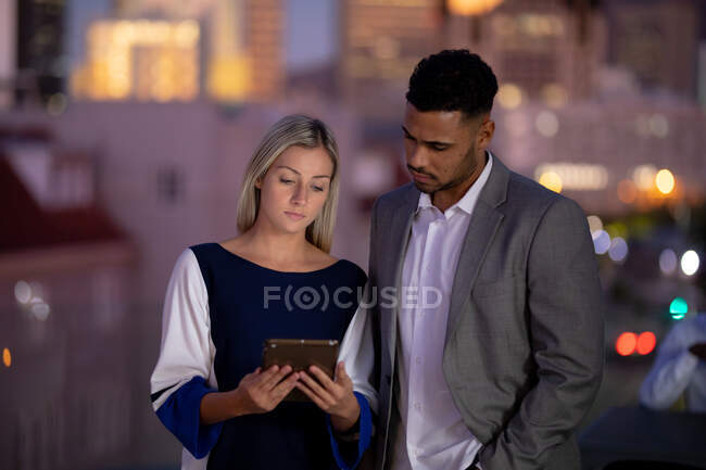 Diversos colegas de negócios masculinos e femininos que trabalham à noite usando tablet e conversando. trabalhando até tarde em negócios em um escritório moderno. — Fotografia de Stock