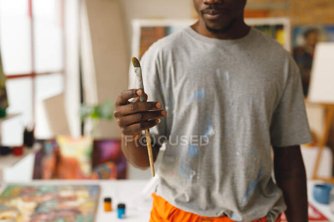 Pintor afroamericano en el trabajo sosteniendo pincel en el estudio de arte. creación e inspiración en un estudio de pintura de artistas. - foto de stock