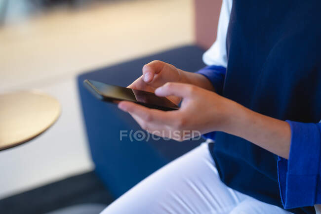 Geschäftsfrau sitzt auf Couch und nutzt Smartphone. Arbeit in einem modernen Büro. — Stockfoto