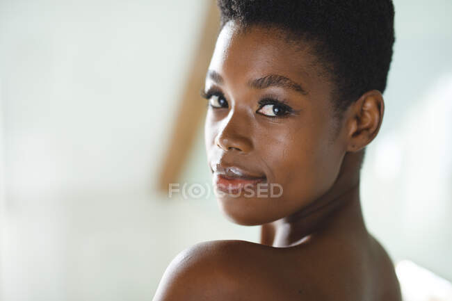 Retrato de una mujer afroamericana sonriente en el baño mirando a la cámara. estilo de vida doméstico, disfrutando del tiempo libre en casa. - foto de stock