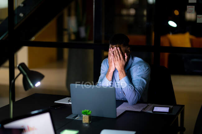 Змішаний гоночний бізнесмен працює вночі, сидячи за столом і використовуючи ноутбук. робота пізно в бізнесі в сучасному офісі . — стокове фото
