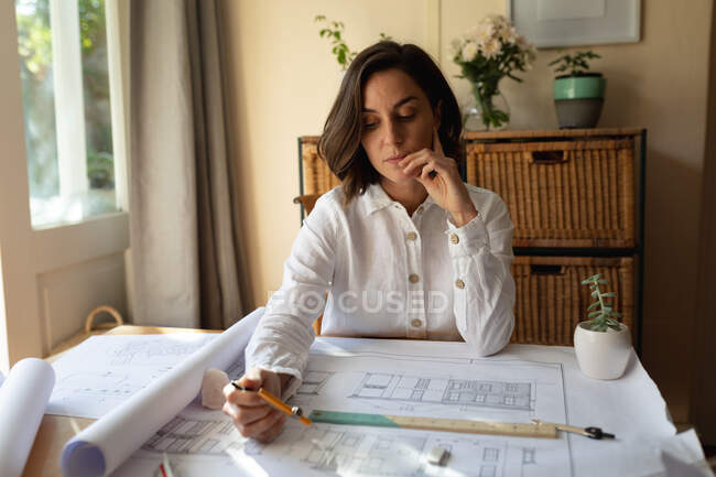 Mulher branca na sala de estar, sentada à mesa a trabalhar, a desenhar planos. estilo de vida doméstico, trabalho remoto de casa. — Fotografia de Stock
