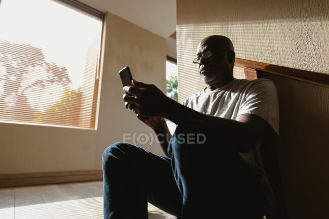 Думливий старший афроамериканець сидить на сходах і користується смартфоном. Життя на пенсії, перебування вдома наодинці.. — стокове фото