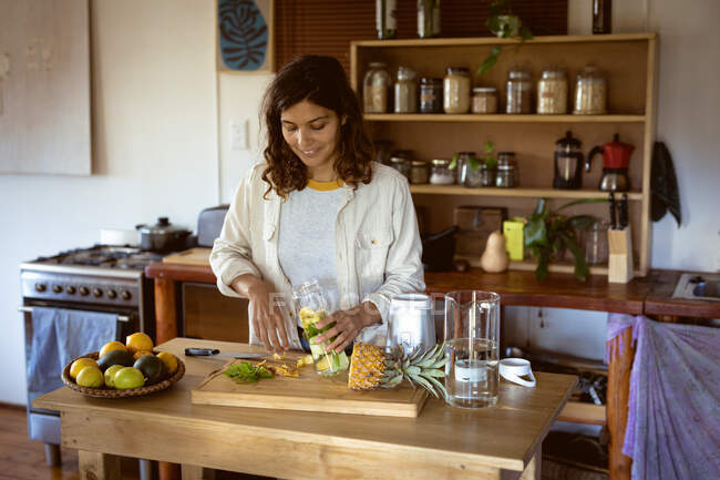 Змішана расова жінка готує здоровий напій на кухні. здоровий спосіб життя, насолоджуючись дозвіллям вдома . — стокове фото