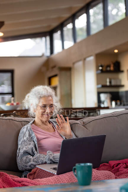 Mulher caucasiana sênior sentada no sofá e fazendo videochamada na moderna sala de estar. estilo de vida aposentadoria, passar o tempo sozinho em casa. — Fotografia de Stock