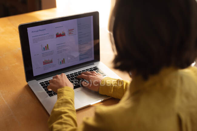 Mulher caucasiana na sala de estar sentada à mesa, trabalhando com laptop. estilo de vida doméstico, trabalho remoto de casa. — Fotografia de Stock
