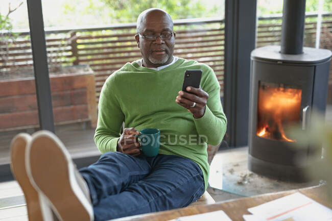 Relaxante homem americano africano sênior situado e usando smartphone na sala de estar moderna. estilo de vida aposentadoria, passar o tempo sozinho em casa. — Fotografia de Stock