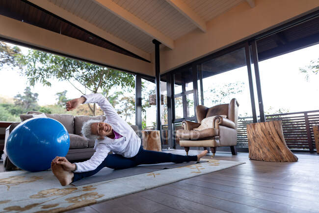 Старша біла жінка у вітальні займається спортом, сидячи на підлозі. пенсійний спосіб життя, проводити час наодинці вдома . — стокове фото