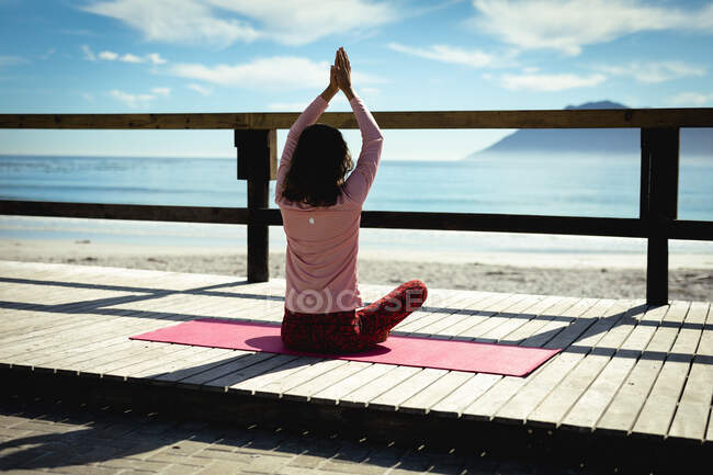 Femme de race mixte pratiquant le yoga le jour ensoleillé au bord de la mer. mode de vie sain, profiter du temps libre à l'extérieur. — Photo de stock